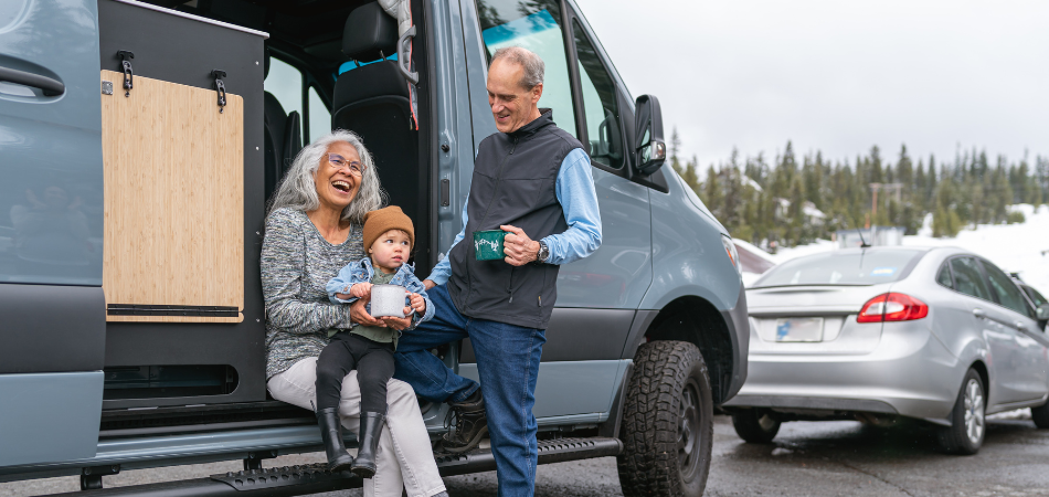 A toddler sitting on his grandparent’s lap in the doorway their motorhome while parked at a skiing resort.