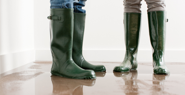 Two people standing side by side with rubber boots on in a a room flooded with water.