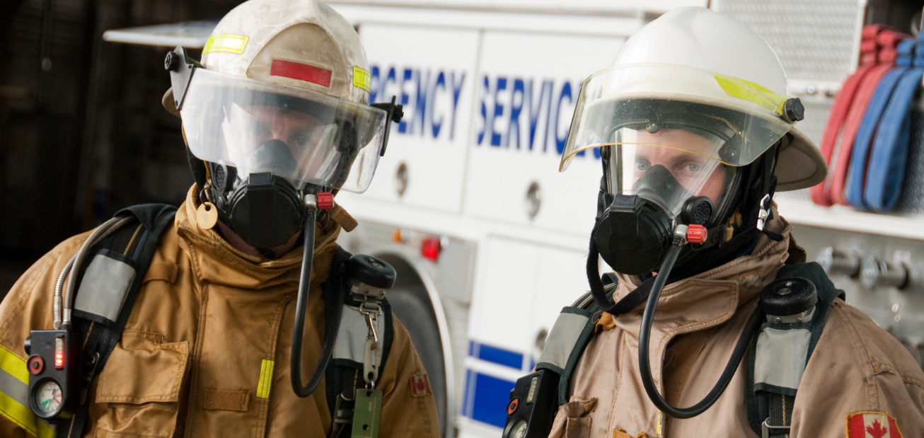 Two Canadian firefighters in front of their firetruck in full gear talking about FireSmart and sharing top fire prevention tips.