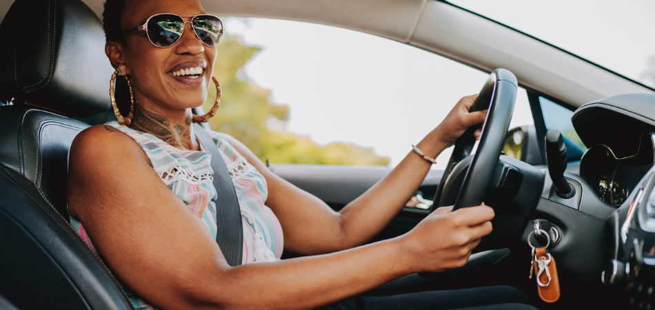 A happy person saving on car maintenance inside their vehicle driving and wearing a sleeveless shirt. 