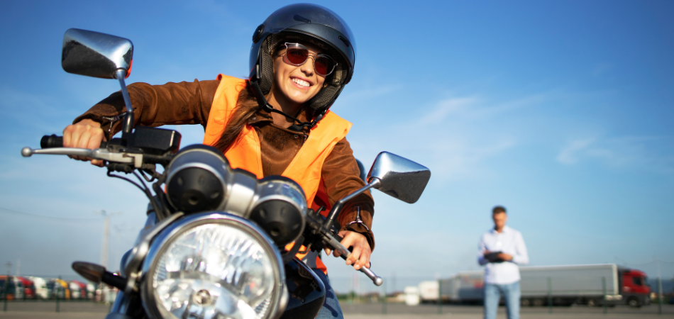 A young woman is seen driving a motorcycle during a motorcycle assessment on a sunny day.