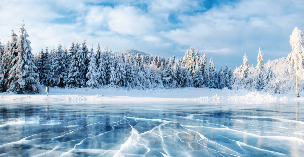 Cracks on the surface of the blue ice. Frozen lake in winter mountains. It is snowing. The hills of pines. Carpathian Ukraine Europe.
