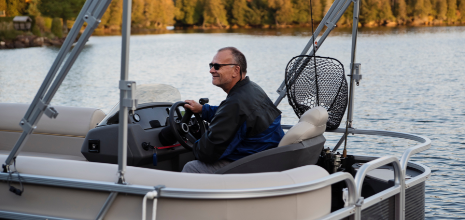 A person is driving a boat with a tree line showing autumn colours in the background.