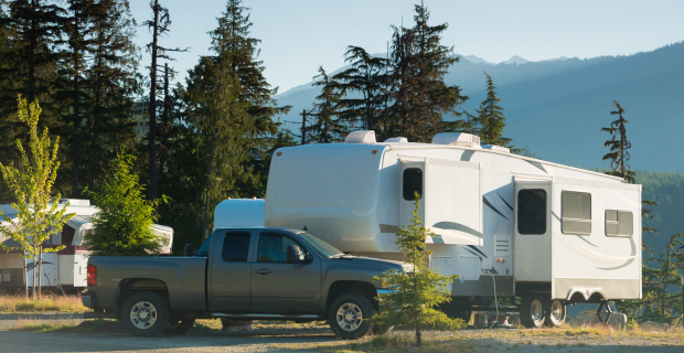 Truck parked in front of a travel trailer in a campground with evergreen trees and a large forest behind them. 