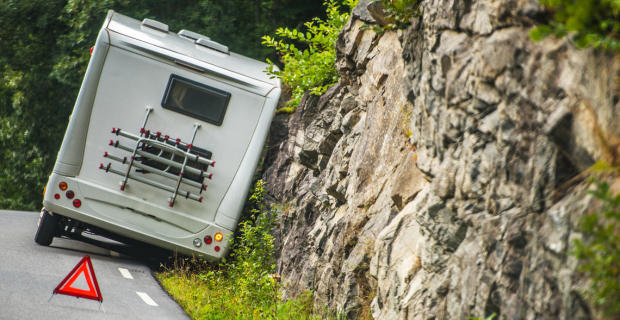 RV pulled off to the side of the road next to a rock wall with an orange pylon in front of the RV to warn drivers.
