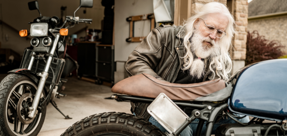 A senior man is seen taking his bike out of his garage and getting it ready with a spring motorcycle checklist.