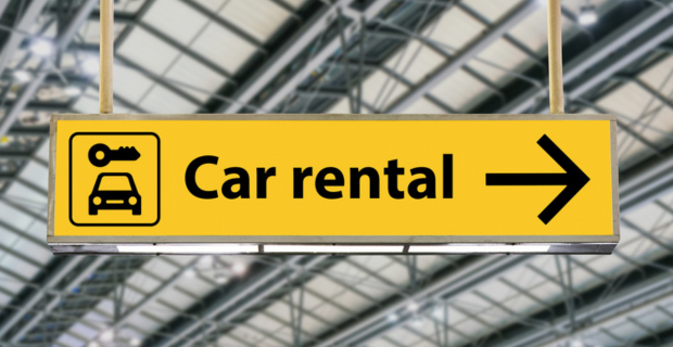 A yellow sign in an airport that has a car and a key on it with the words “car rental” and an arrow.