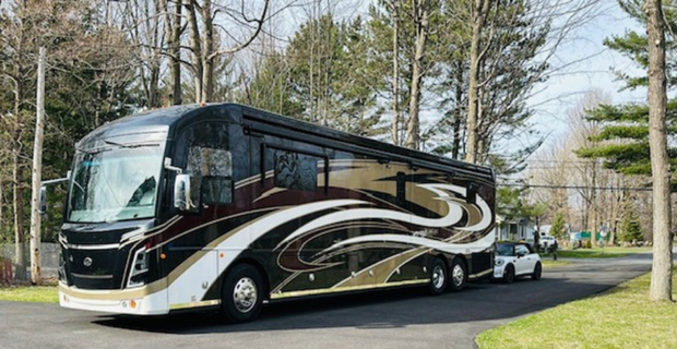 Class A motorhome towing a white car down the road.
