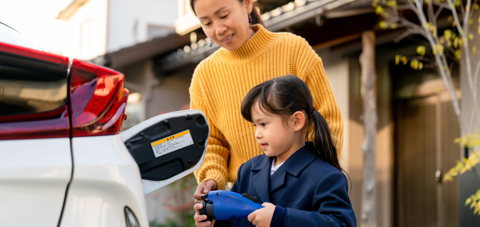 Parent and child charging an electric vehicle at home in a residential driveway.