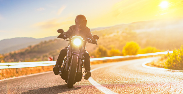 Sunset over an open road and a man with a helmet riding a chopper motorbike.