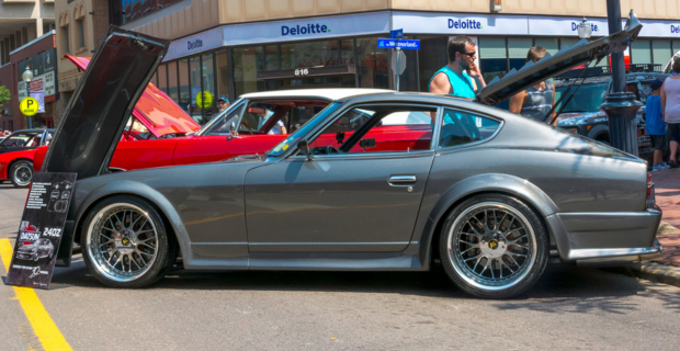 A dark grey 1970 Nissan Datsun 240Z at a car show with the hood up.