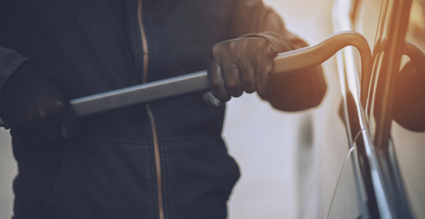 Thief trying to break into a car with a crowbar. 