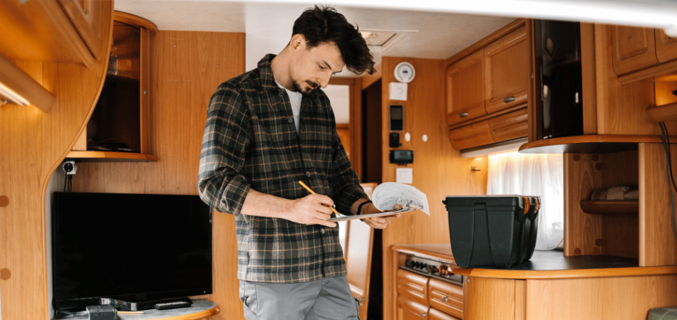 A man standing in his RV with a clipboard working through his spring RV maintenance checklist for the coming season.
