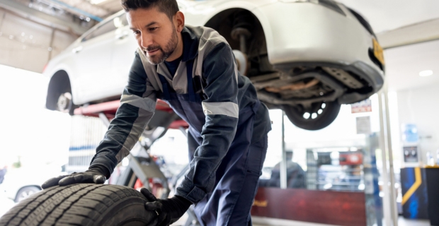 A mechanic walking a car wheel off to the side while changing the tires of a car in their shop. 