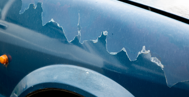 Paint peeling above the wheel well of a blue car from sun damage. 