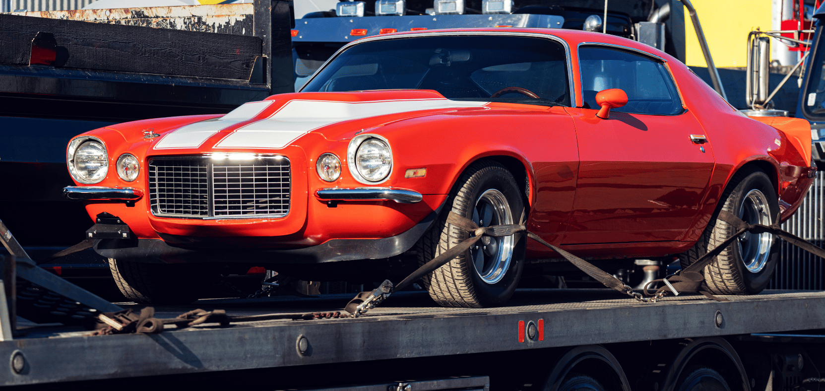 Red 1970s muscle car strapped to a flatbed trailer during transport.