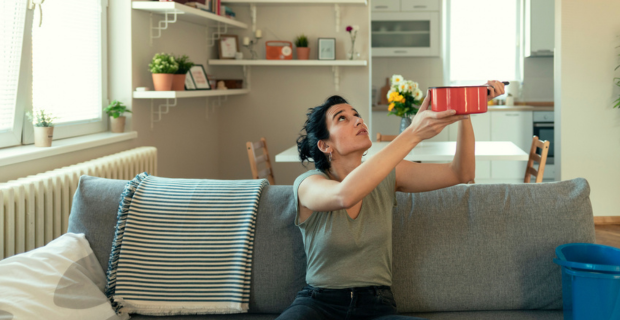 Person sitting on a couch holding a pot up to catch water leaking from ceiling in a condo.