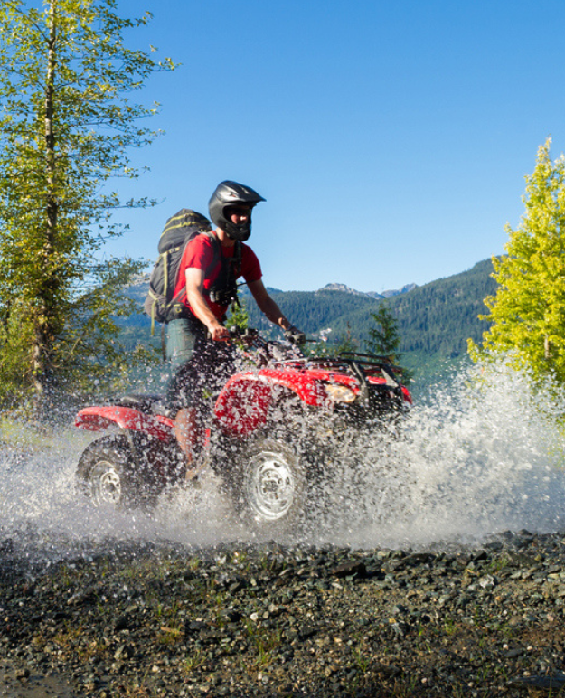 A rider makes a splash riding his four-wheeler through a puddle. 