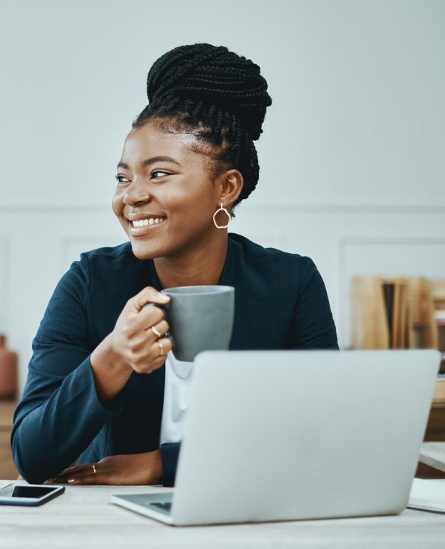 A Black woman sitting at her computer, drinking coffee.