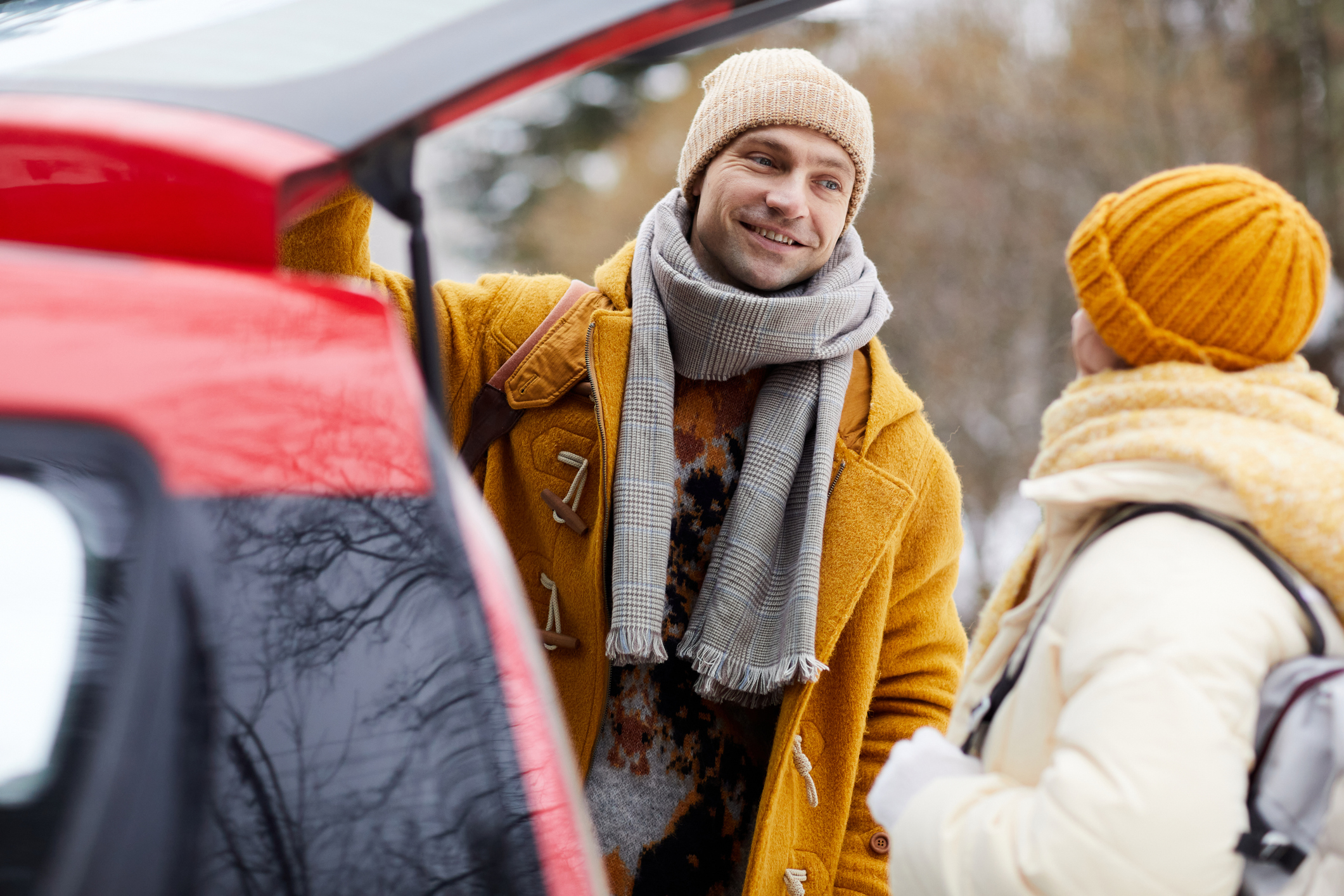 A smiling couple standing at the open trunk of their car in winter