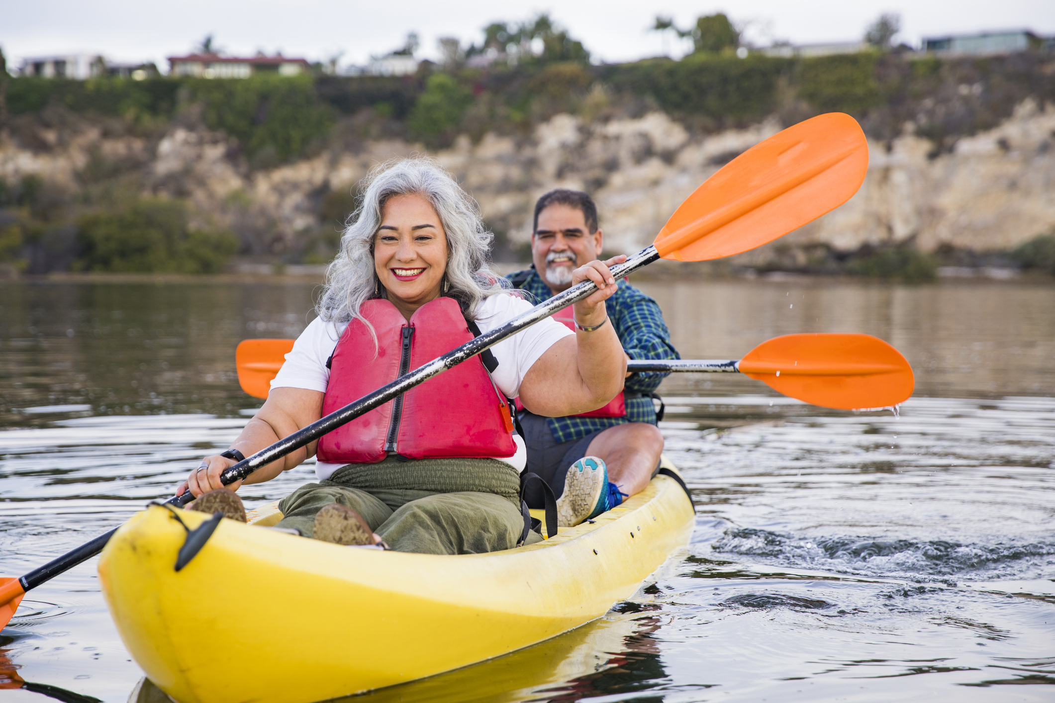A man and woman wearing life jackets and kayaking