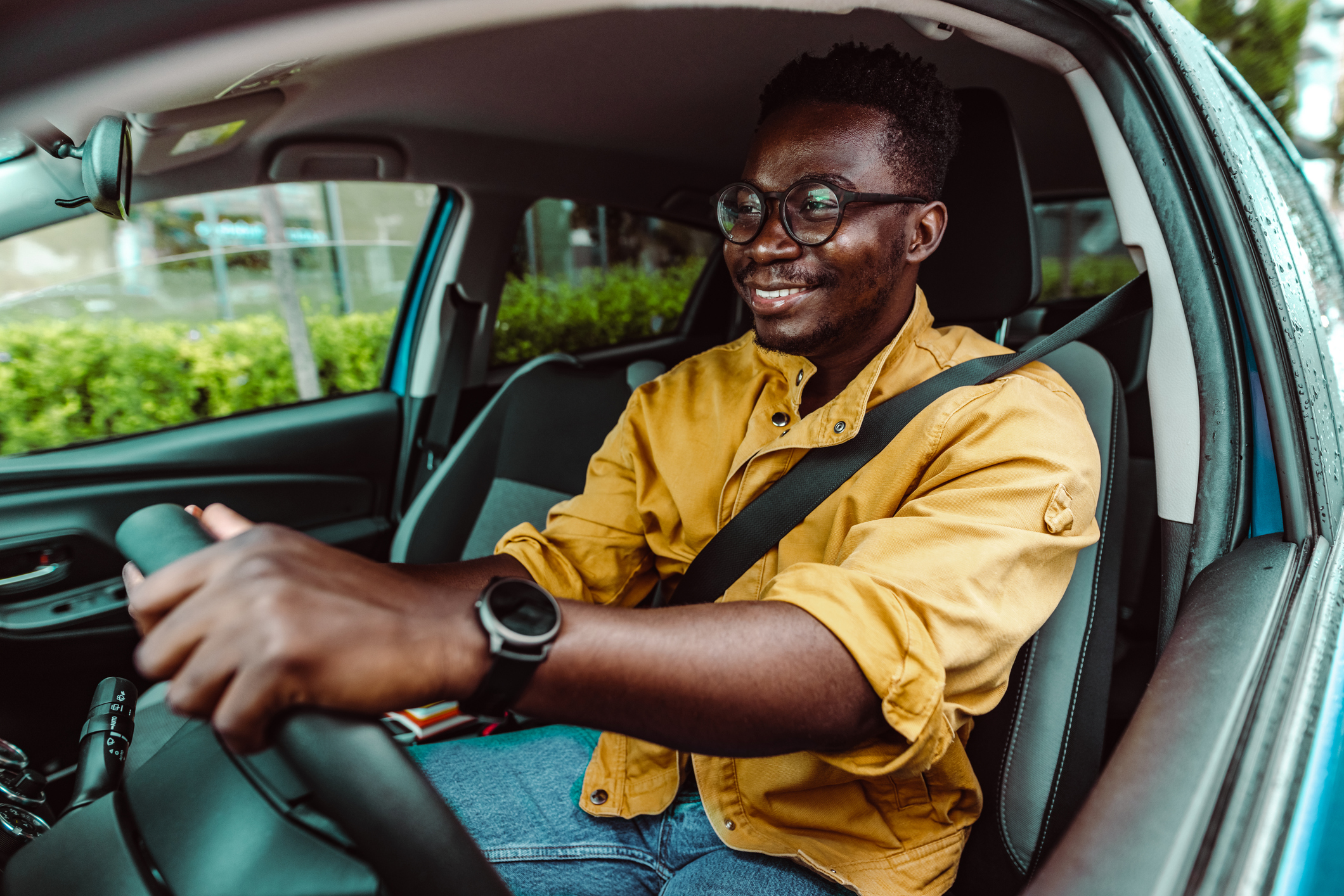 A man wearing glasses is sitting in the driver's seat of his car