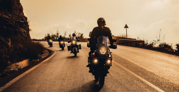 A sepia-toned photo of four riders following safely, one after the other, around a curve in the road.