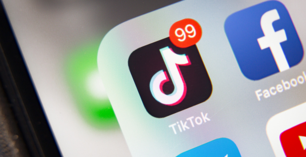 A close-up on the TikTok app icon, with 99 notifications showing, on a smart phone screen. 