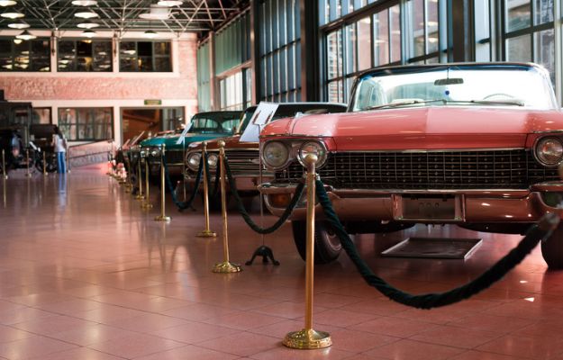 Classic cars are displayed behind velvet ropes at a car museum.