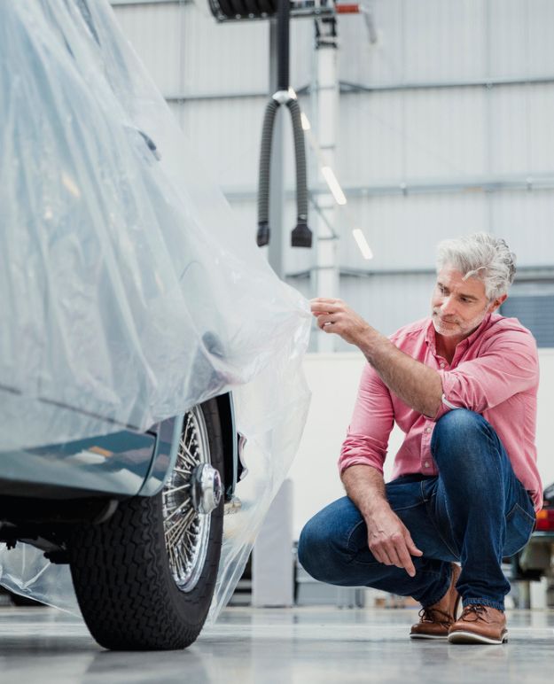 The classic car owner lifts the dust cover to examine the restoration work completed on their car.