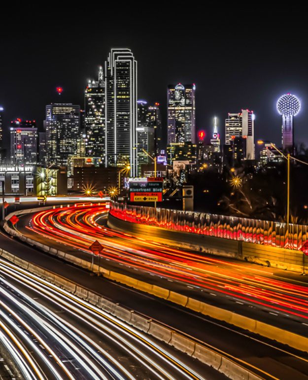 Timelapse streams of headlights and tailights show the way to the colourful night skyline of a large city.