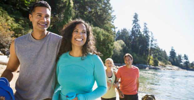 Two couples are walking arm in arm along the edge of a beautiful river on a sunny day in Alberta.