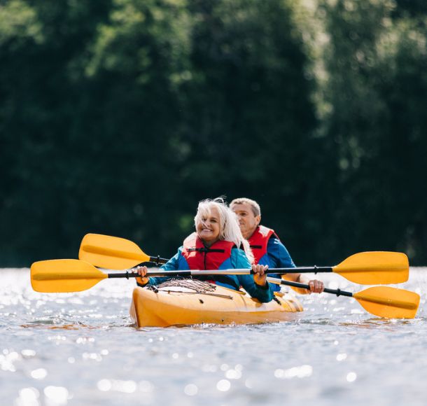 A retired couple paddling a two-person kayak on a sunny summer day in Alberta.