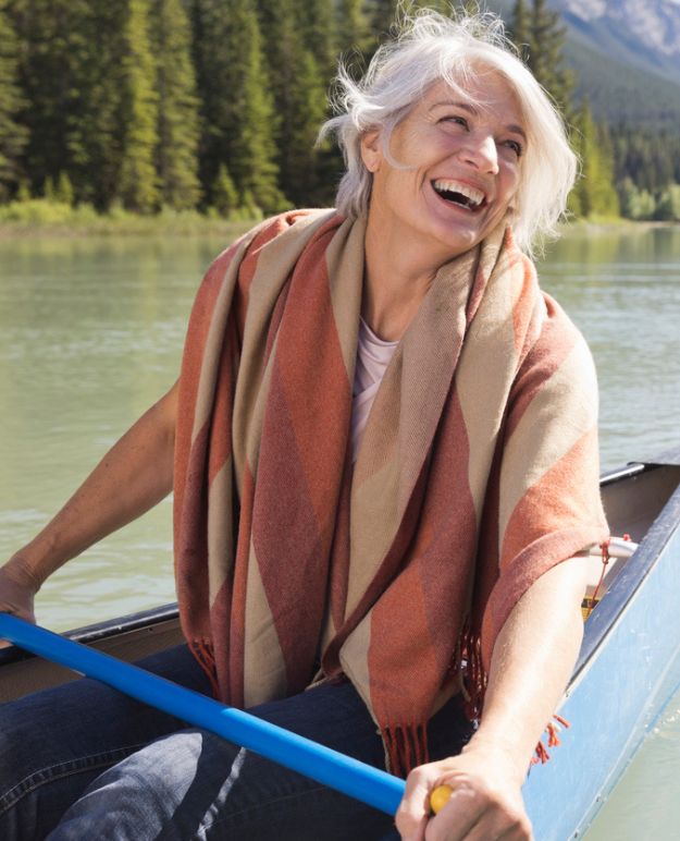 A woman with silver hair laughing and paddling a canoe.