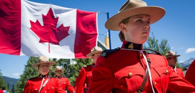 An RCMP Officer marching in a parade with a Canadian flag waving behind them. 