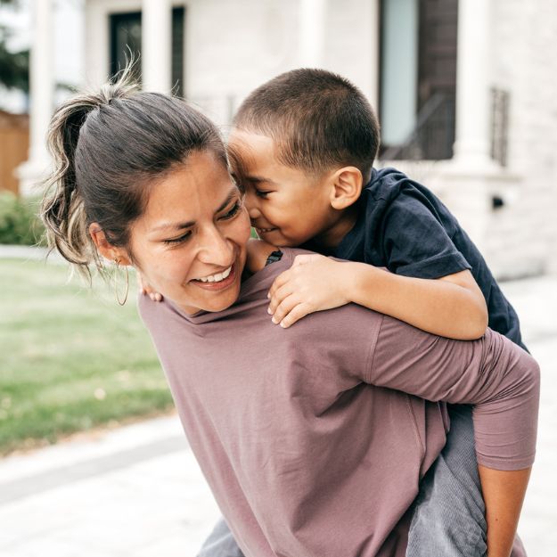 A parent gives her son a piggyback in their driveway. 