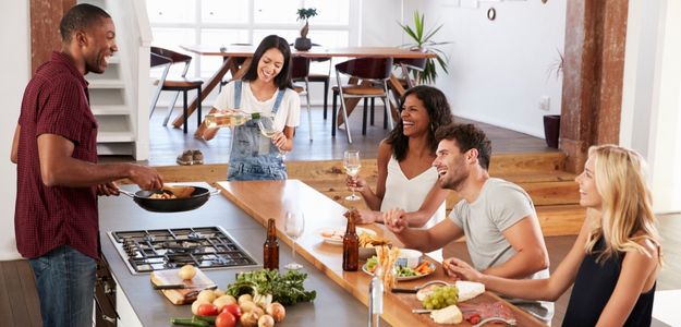 A group of five friends gathered around a kitchen island enjoying lively conversation.