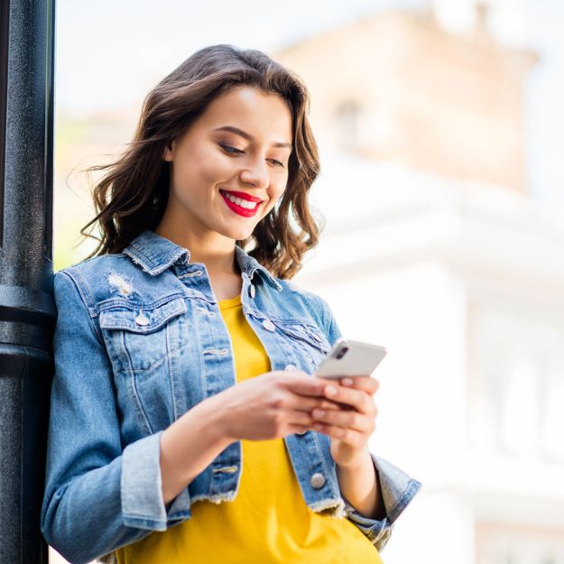 A  woman leaning against a light pole, checking a message on her phone.