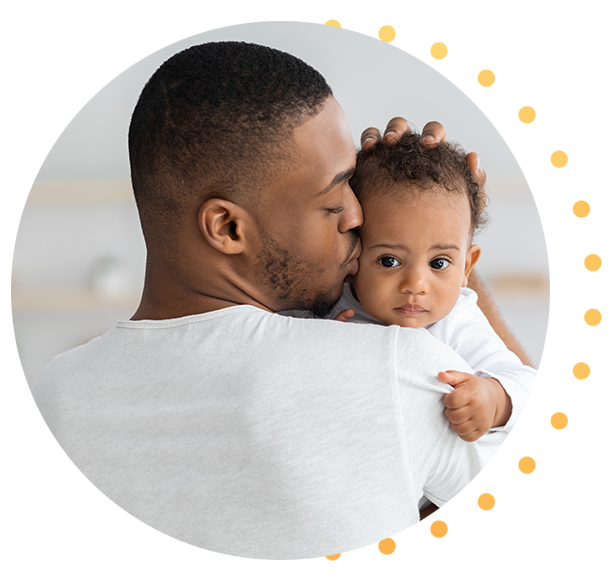 A Black father giving his baby a kiss on the cheek while holding them in his arms.