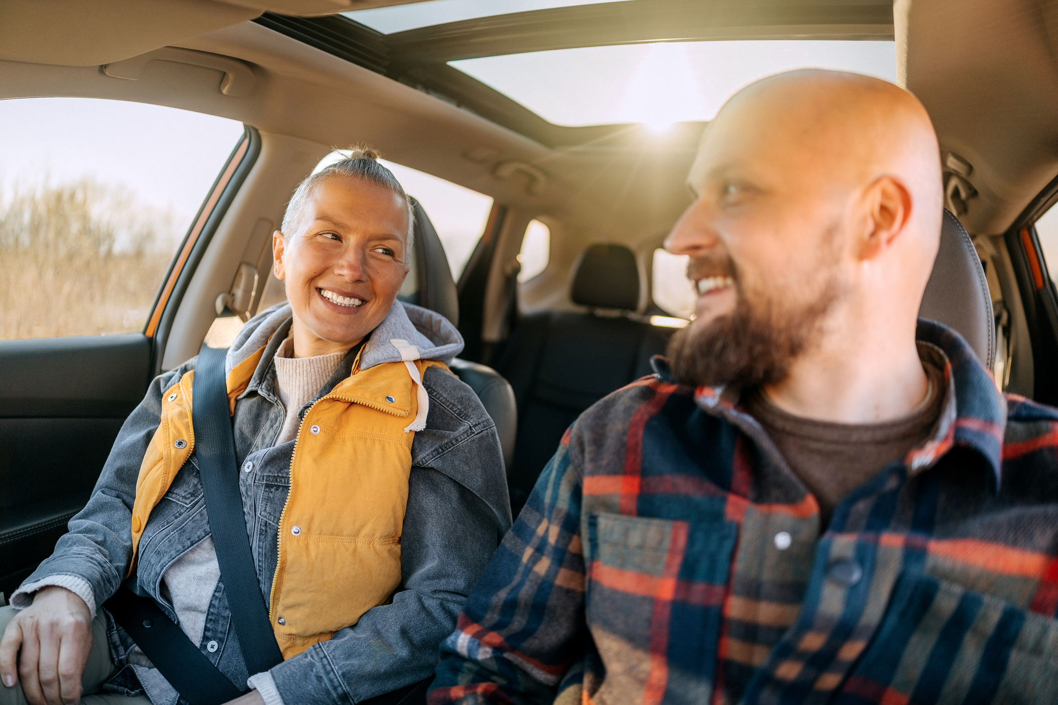 Smiling man and woman driving in car with sunroof open