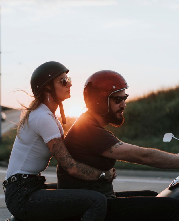 A man and woman riding on a cruiser, the sun setting behind them.