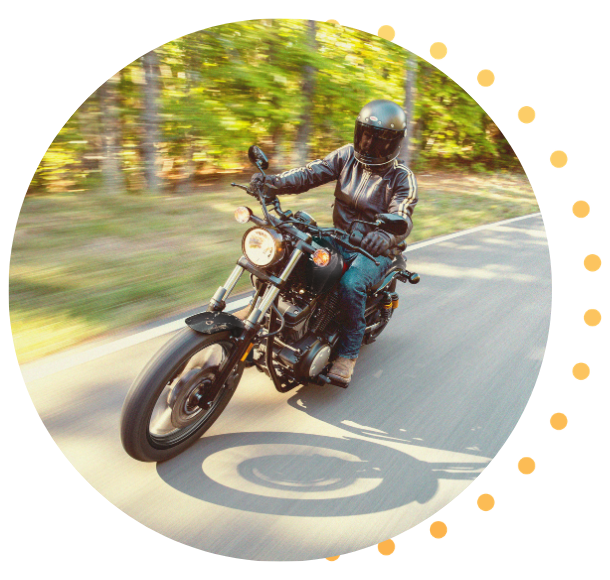 A person wearing protective gear rides a motorcycle on a tree-lined road, with motion blur showing the bike moving at speed.
