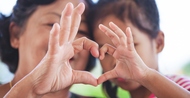 An adult and child join their hands together into a heart shape.