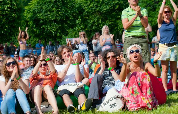 A group at an outdoor event sits on the grass clapping.