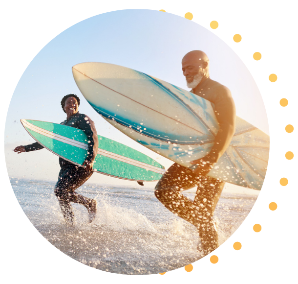 A Black couple in their early 50's running in the surf, carrying surfboards under their arms.