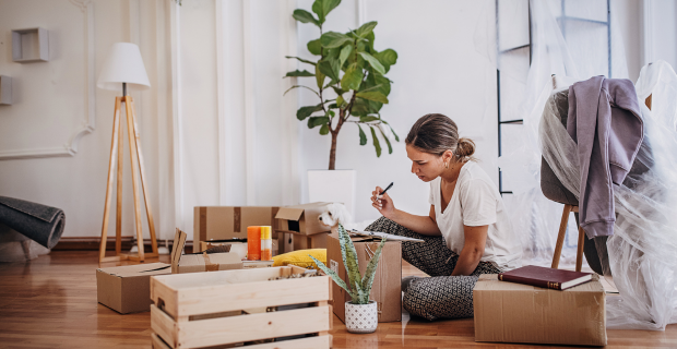 A young adult sitting on the floor in her new home and creating a home inventory list of belongings. 