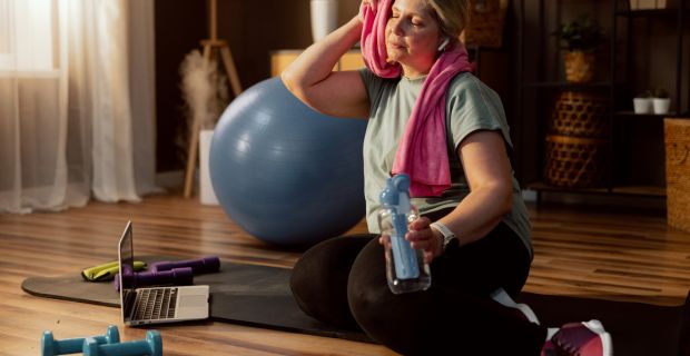 A woman in her mid-40s wipes sweat from her forehead after finishing a great home workout. 