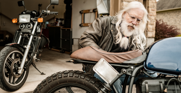 A senior man is seen taking his bike out of his garage and getting it ready with a spring motorcycle checklist.