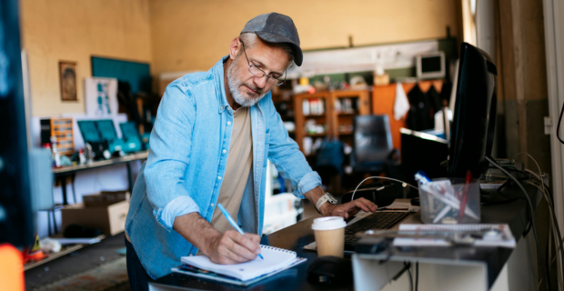 A mature man is in his workshop writing down notes and planning for 2026 business insurance trends.  
