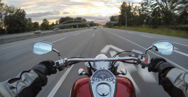 A person on a motorcycle is driving down the highway on a partially cloudy day. The photo is taken from the driver’s perspective. 